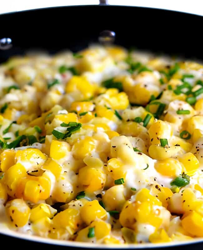 a close up image of cream cheese corn scattered with chopped fresh herbs.