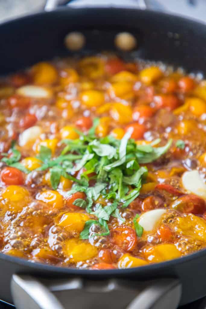 herbs added to tomatoes in a pan