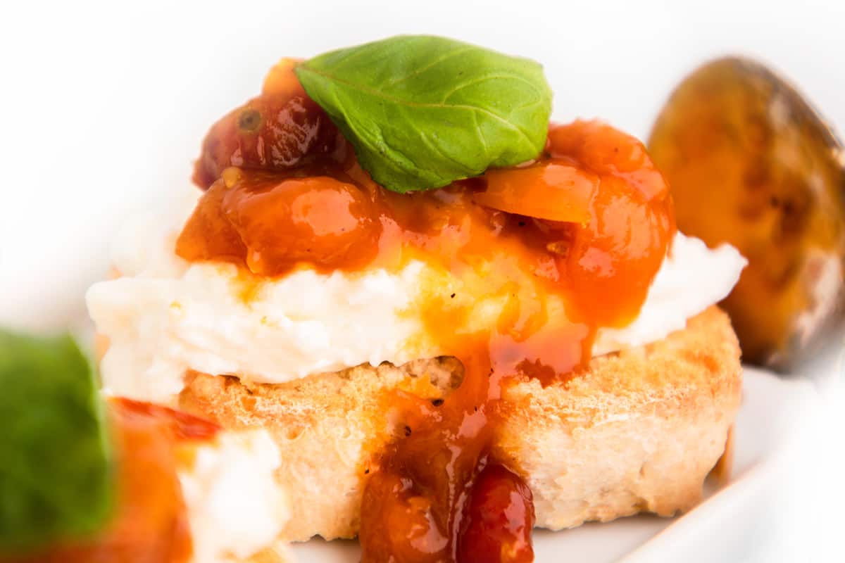 close up of Crostini with burrata cheese, tomato jam and basil