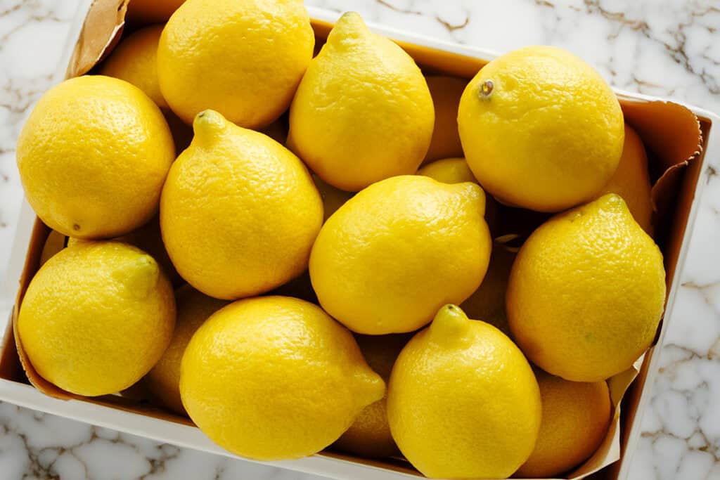 A crate of lemons on a marble countertop.