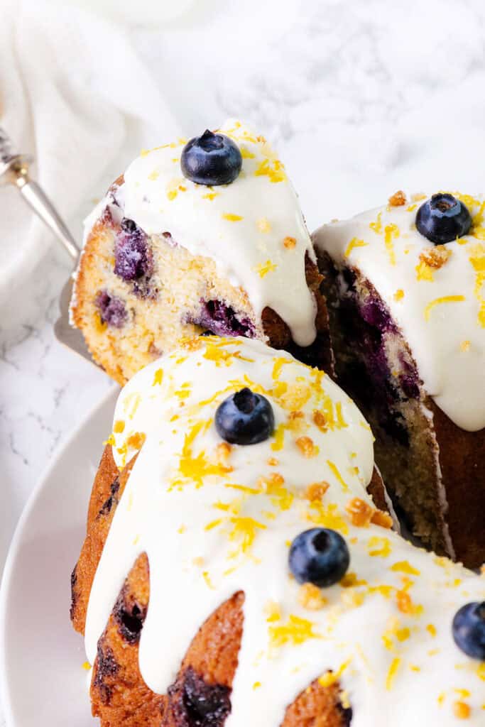 A close-up slice of lemon blueberry bundt cake on a plate with a spatula holding one slice.