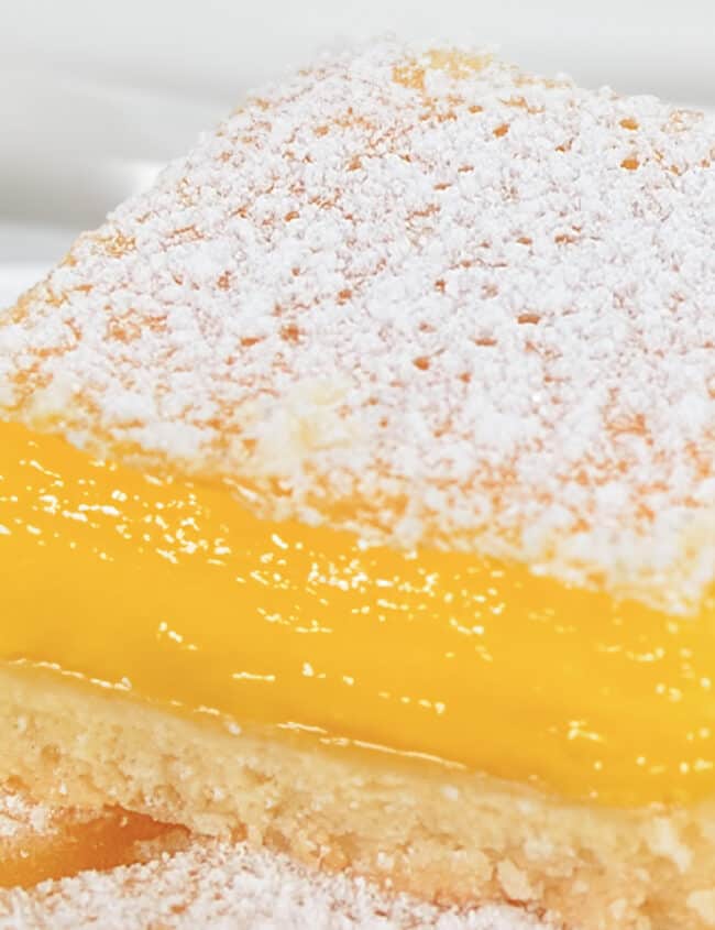 A close up image of a stack of lemon squares on a white plate.