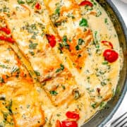 a pan of three salmon fillets in a cream sauce with tomatoes and spinach