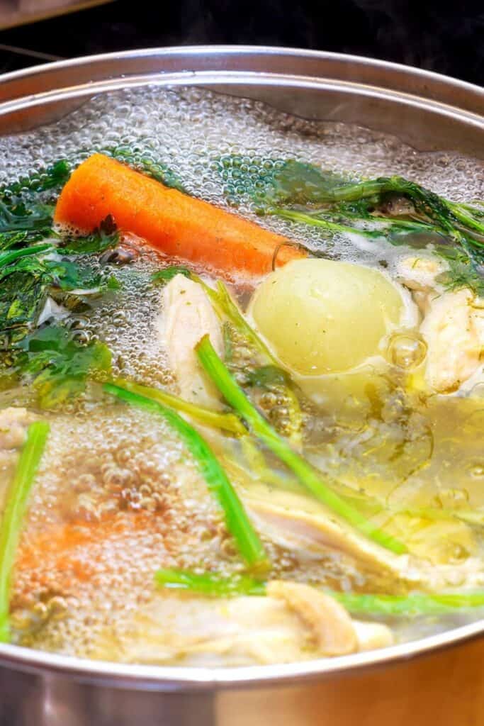 Ingredients for preparing chicken bone broth in a pot - chicken, onions, celery root, carrots, parsley