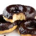 a pile of Chocolate frosted donuts with the top one missing a bite