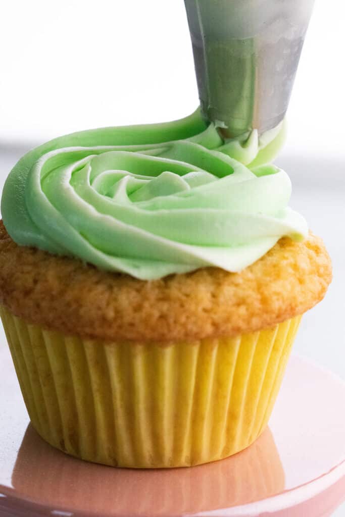 a piping bag swirling frosting onto a cupcake