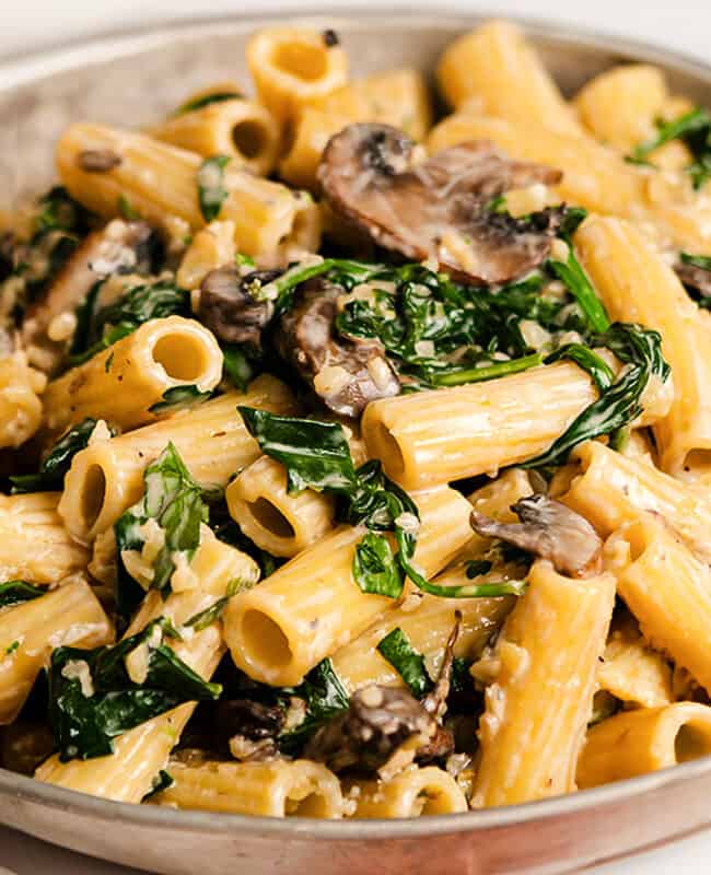 A close up image of pasta in a creamy sauce with mushrooms and spinach.