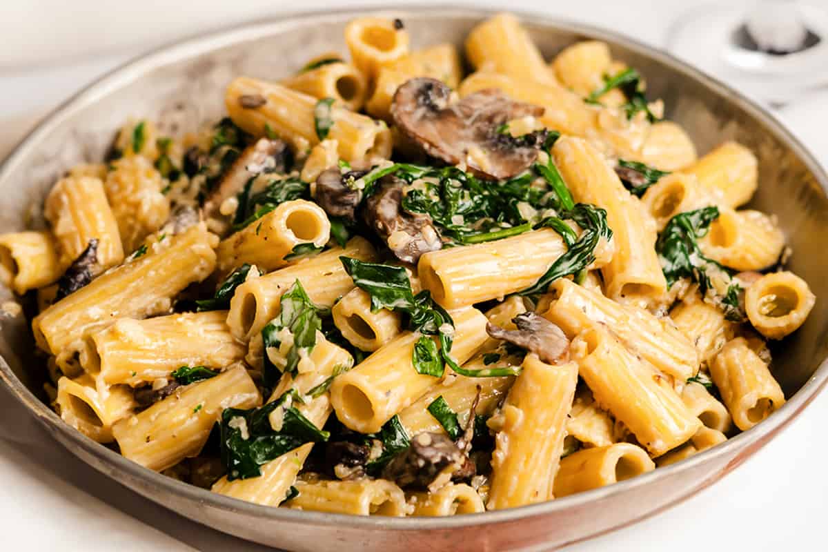 A close up image of pasta in a creamy sauce with mushrooms and spinach.