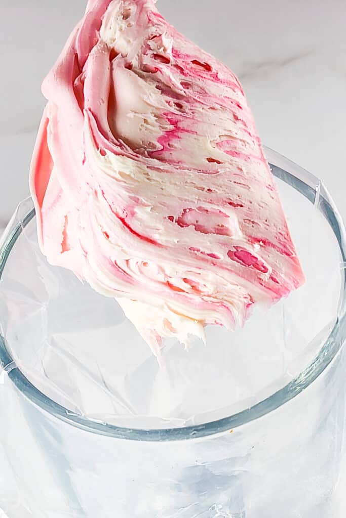 white frosting streaked with pink on a spatula