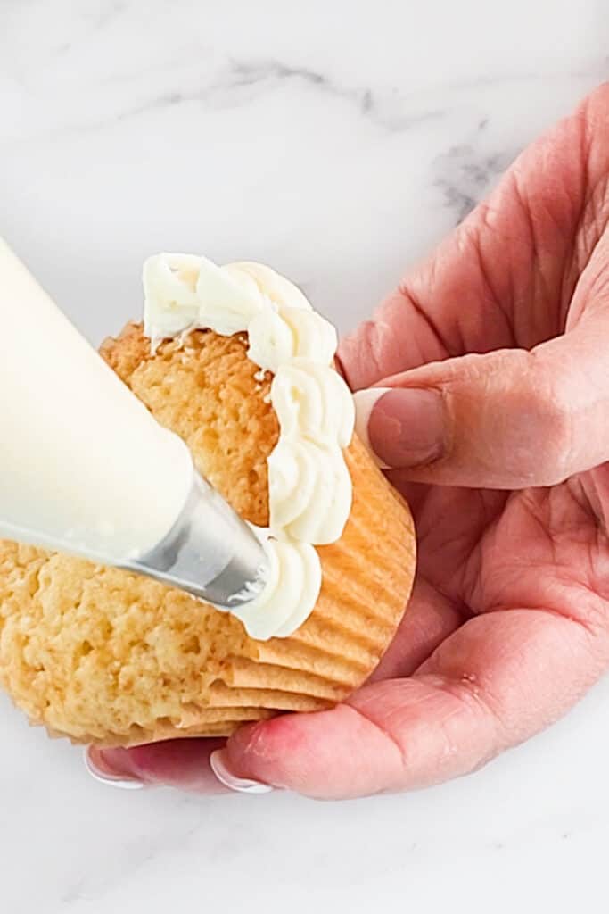 a piping bag piping a flower onto a cupcake