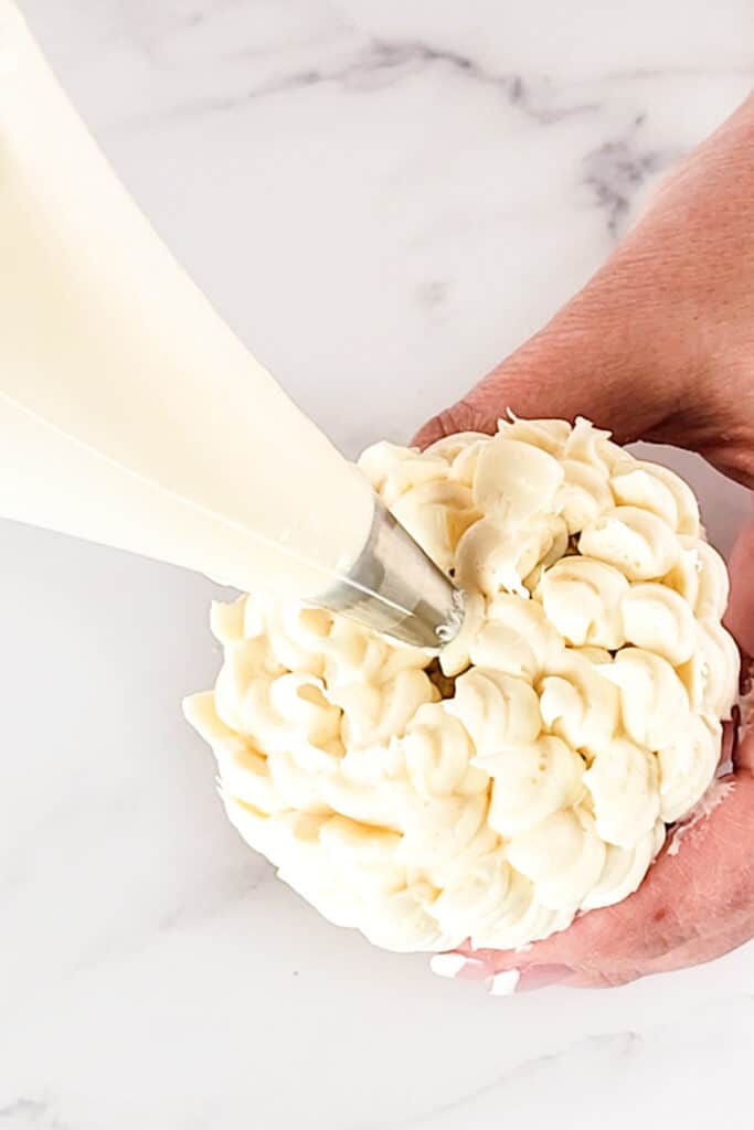 a white flower being piped onto a cupcake with a piping bag