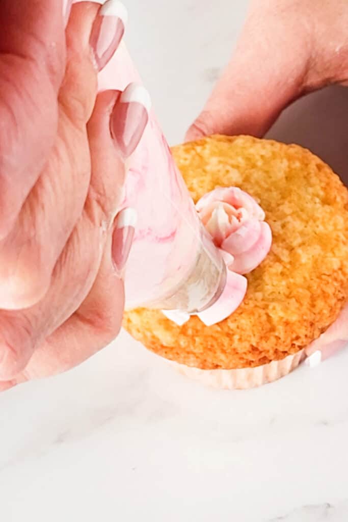 a pink flower being piped onto a cupcake