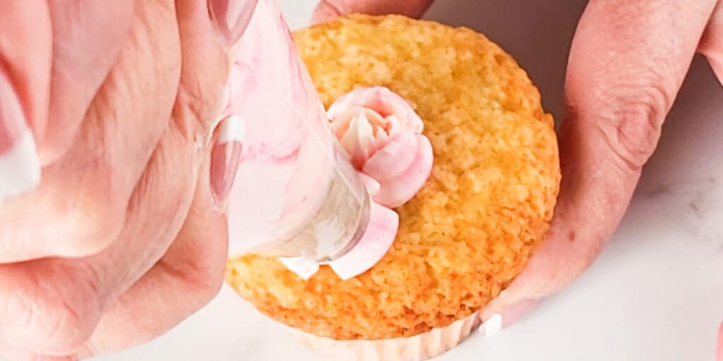 a flower being piped onto a cupcake