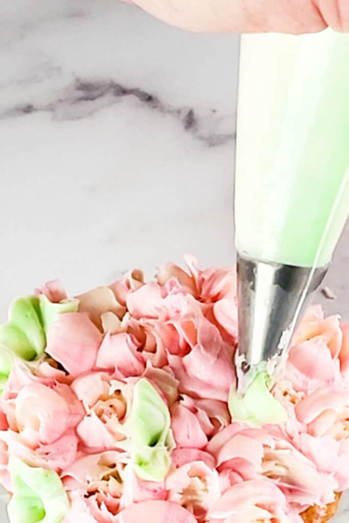 a piping bag piping leaves onto a cupcake with flowers