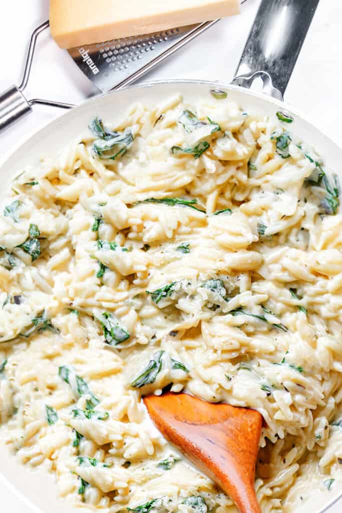 a close up of creamy orzo and spinach with a wooden spoon.