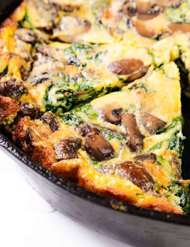 A close up image of a Easy Spinach Mushroom Frittata with a slice cut in a skillet.