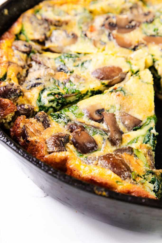 A close up image of a Easy Spinach Mushroom Frittata with a slice cut in a skillet.