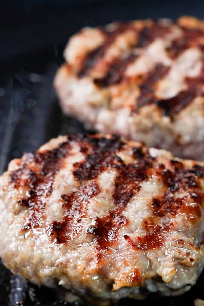 two pork burgers cooking on a grill pan