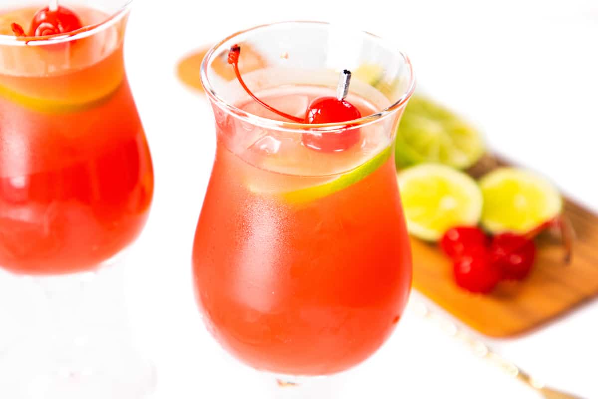 Two sea breeze cocktails with a garnish of cherries and lime slices with more fruit in the background.