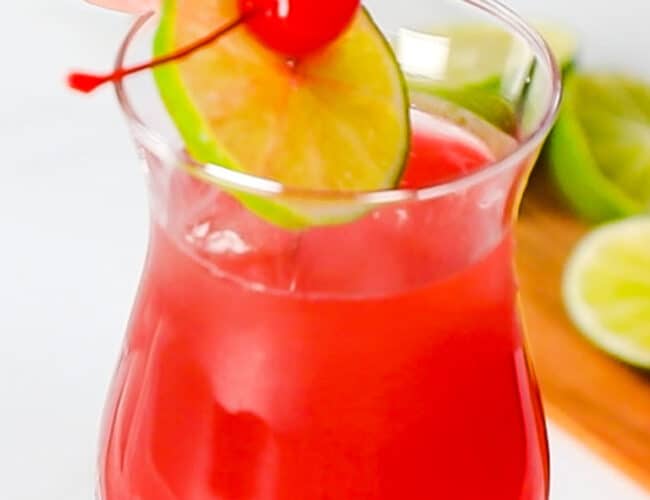 a maraschino cherry and lime slice being placed in a sea breeze cocktail