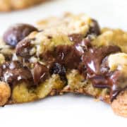 Close-up of a gooey chocolate chip cookie with melted chocolate oozing from the center. The easy chocolate chip oatmeal cookie appears freshly baked, with a golden-brown, slightly crispy exterior.