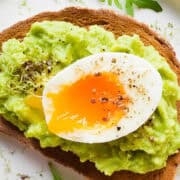 A plate with a slice of toasted bread topped with Guacamole and a halved soft-boiled egg, garnished with freshly ground black pepper and green herbs.