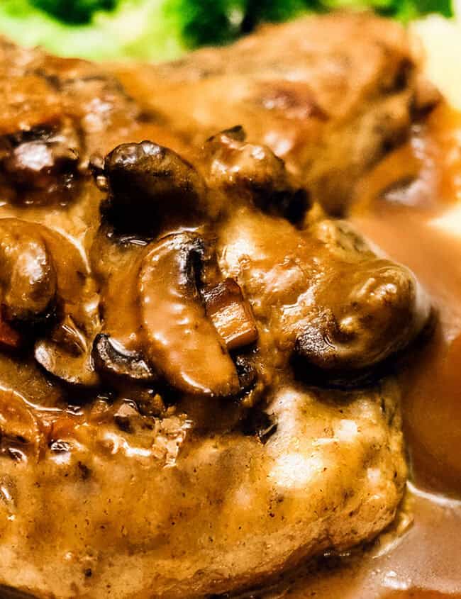 A plate of mashed potatoes and pork chops smothered in mushroom gravy, served with a side of steamed broccoli, reminiscent of classic smothered pork chops.