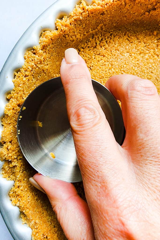 Graham Cracker Crust being pressed into a pan with a cup