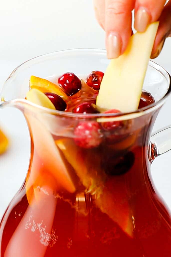 a woman adding an apple slice to the sangria