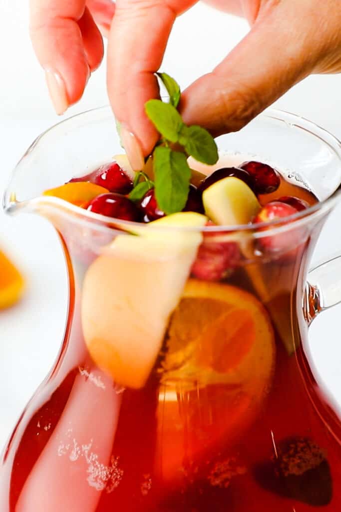 a woman adding mint to the sangria topped with fruit.