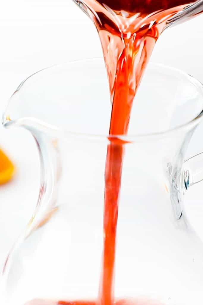 the cranberry juice mixture being poured into a glass pitcher.