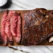 A wooden board on a marble surface with perfectly pan-fried steak, with three medium-rare slices.