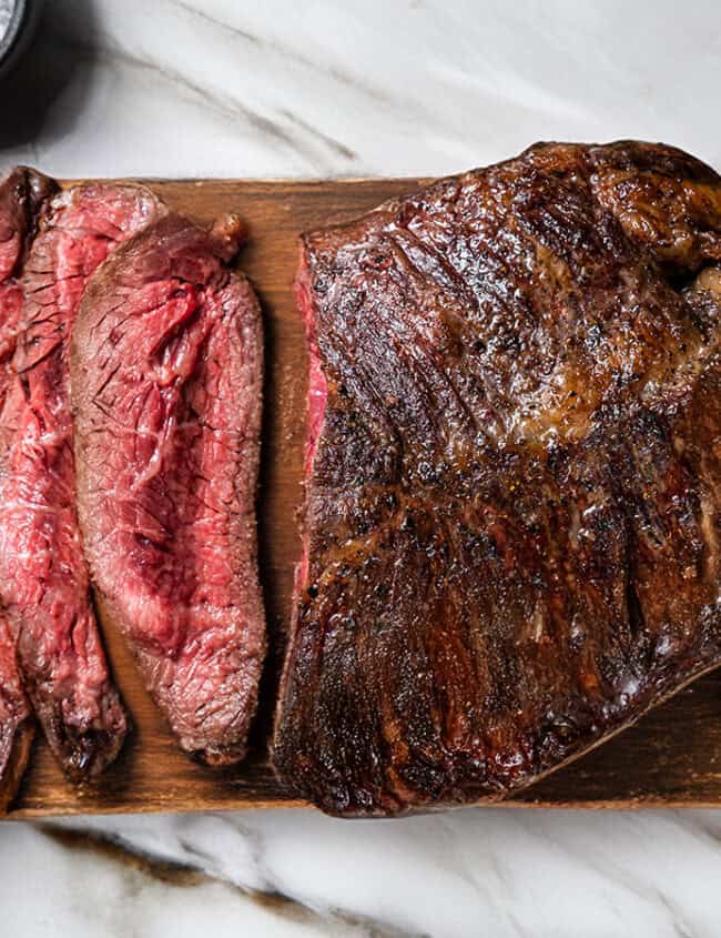 A wooden board on a marble surface with perfectly pan-fried steak, with three medium-rare slices.