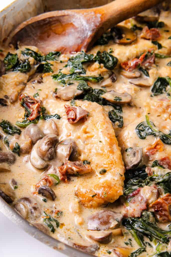 Close-up of Tuscan chicken with sun-dried tomatoes, spinach, and mushrooms in a creamy sauce.