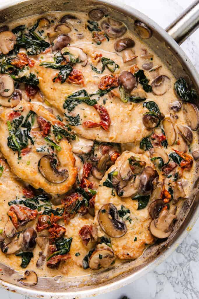 Pan of creamy Tuscan chicken with sun-dried tomatoes, spinach, and mushrooms, showcasing a rich and flavorful sauce.