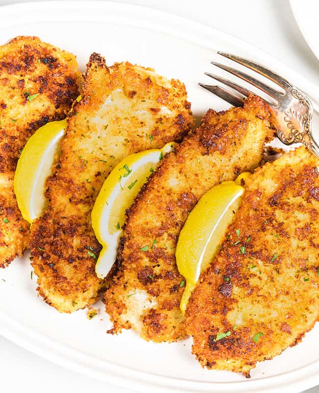 an overhead image of Panko Chicken on a plate with a fork and lemon wedges