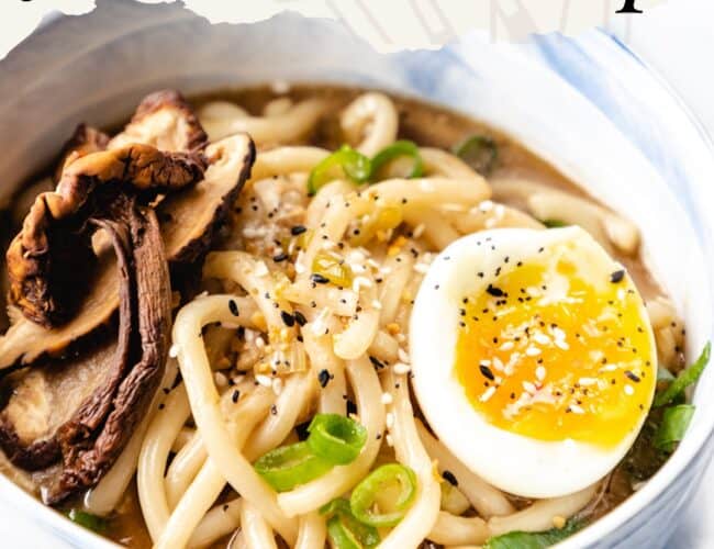 A photo of udon noodle soup with egg, scallions and sesame seeds on top