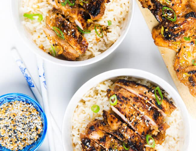 two bowls of rice topped with sliced miso chicken garnished with green onions and sesame seeds