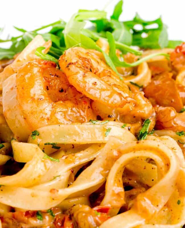 a landscape image of a white plate full of shrimp pasta