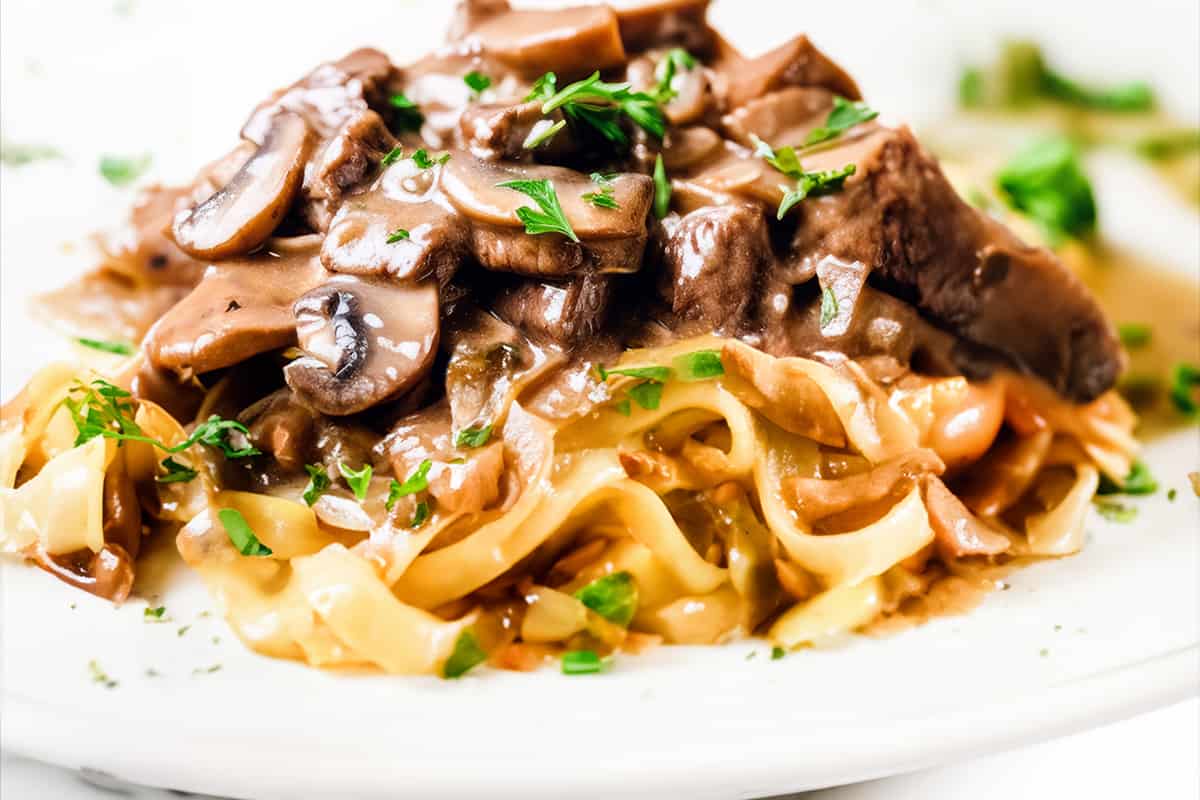 a close up image of Beef Stroganoff made up of Beef and mushrooms in a creamy Stroganoff sauce over noodles.
