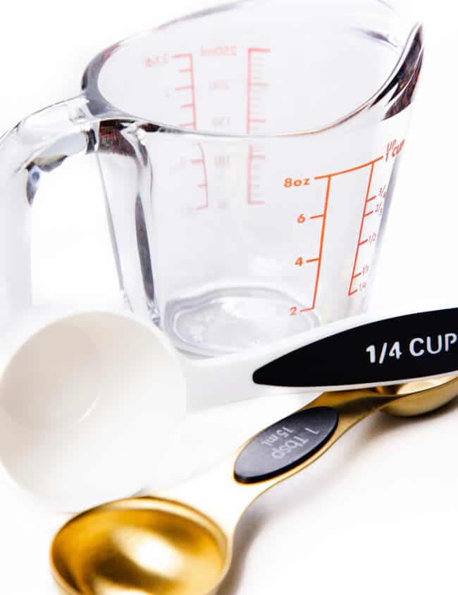 a photo showing a glass measuring cup, a plastic 1/4 cup measuring cup and a gold tablespoon measuring spoon