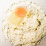 An egg in a mixing bowl with creamed butter and sugar.