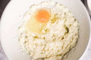 An egg in a mixing bowl with creamed butter and sugar.