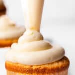 A close-up of a Key Lime Cupcake being frosted with creamy icing, showcasing the smooth and rich texture of the frosting with other frosted cupcakes blurred in the background.