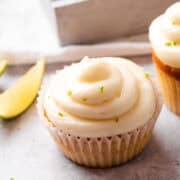 Two Key Lime Cupcakes topped with creamy frosting and garnished with lime zest, with lime wedges in the background.