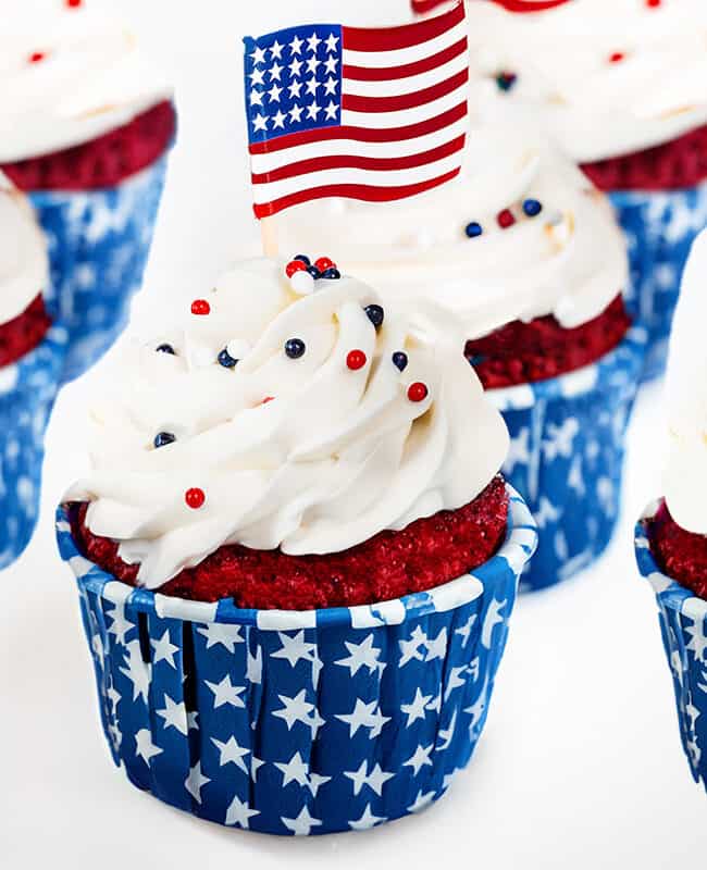 a group of 4th of July Cupcakes topped with American flags and red, white, and blue, decoration.