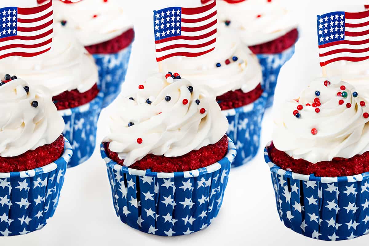 a group of 4th of July Cupcakes topped with American flags and red, white, and blue, decoration.