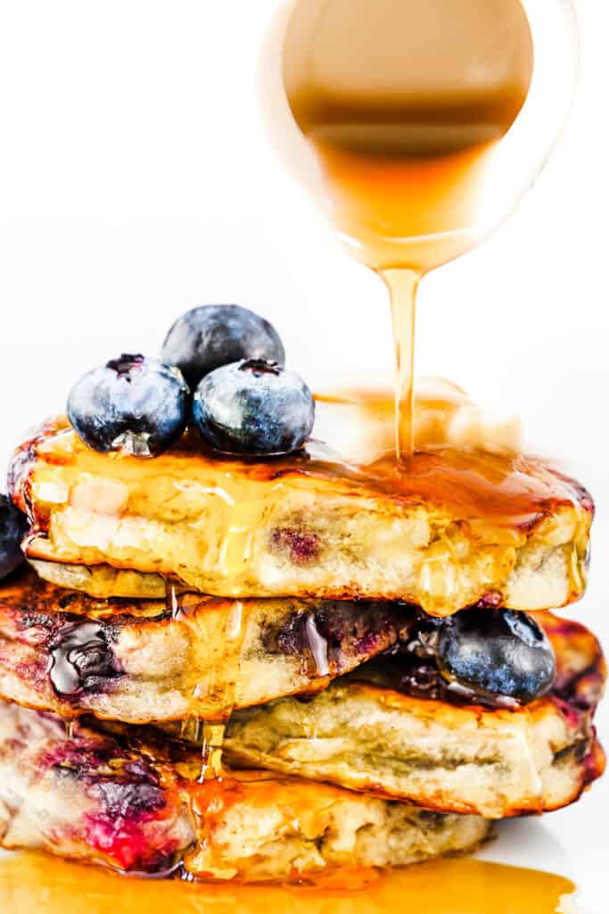 a stack of blueberry pancakes with syrup being poured on top