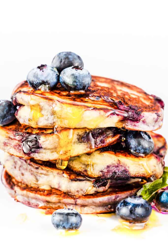 Blueberry pancakes dripping with syrup and topped with fresh blueberries.