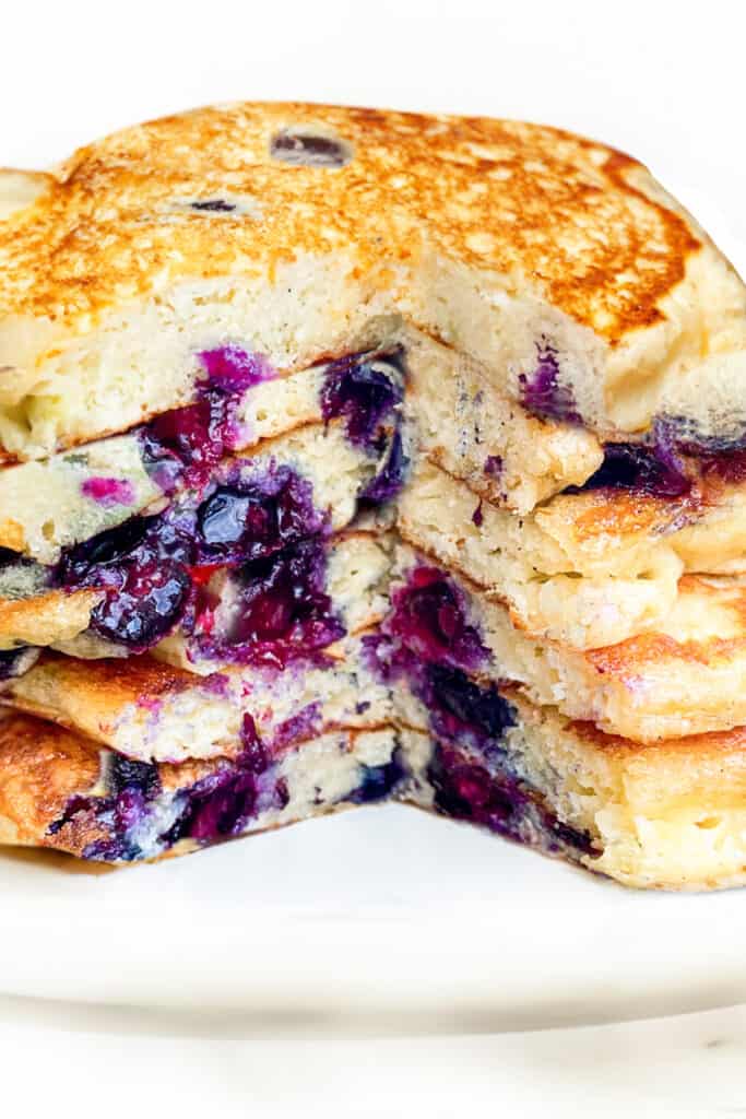 a stack of Blueberry Pancakes with a wedge cut down the middle to show the fluffy interior.